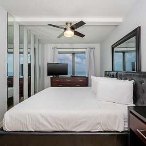 The master bedroom features a plush bed, a large window with a stunning beachfront view, and modern furnishings