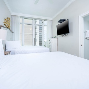 Inviting guest bedroom featuring two queen beds, a TV, and large windows that fill the space with light