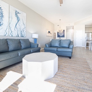 Light-filled living area features two blue leather sofas, a unique white coffee table, and a view into the modern kitchen
