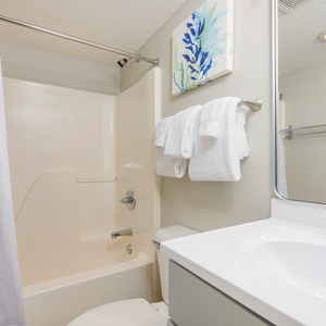 Soft towels await after your refreshing shower in the full bath with a tub shower combo and coastal art
