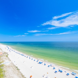 Coastal view with soft white sands and vibrant blue umbrellas under a clear blue sky, perfect for relaxation