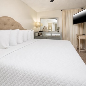 Inviting bedroom featuring a king bed with crisp white linens, a stylish mirrored dresser, and a mounted flat-screen TV