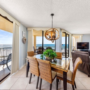 Bright dining area with chairs and a view of the beach, featuring a modern chandelier and a cozy living space nearby