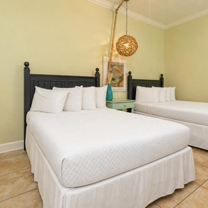 This cozy guest bedroom features two full beds with white linens, a charming teal nightstand, and a unique pendant light