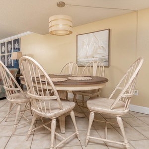 This dining area features a round wooden table with six charming whitewashed chairs, perfect for family meals