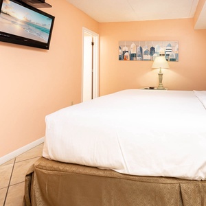 Relaxing guest bedroom featuring a king bed, soft peach walls, and a mounted TV for your entertainment