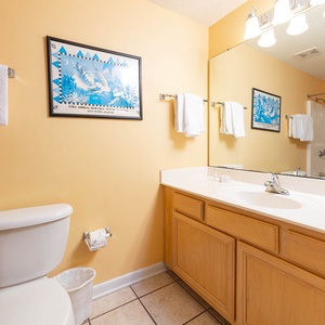 Refresh in this guest bathroom featuring a spacious vanity, cheerful yellow walls, tub-shower, and coastal artwork