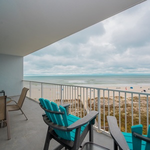Enjoy a relaxing view from the balcony with turquoise chairs overlooking the beach and inviting sandy shores