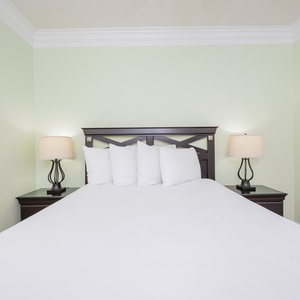Rest in this serene guest bedroom featuring a queen bed, soft linens, and calming green walls for a peaceful getaway