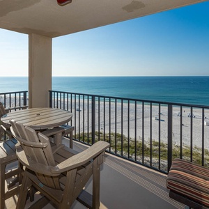 A spacious balcony features a round table and chairs, offering a serene view of the beach and calm blue waters