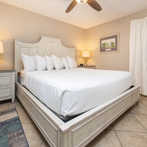 Brightly lit bedroom featuring a plush king bed with decorative pillows, a bedside lamp, and soft neutral tones throughout