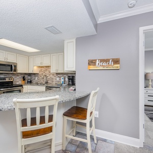 Modern kitchen features granite countertops, bar seating, and a welcoming decor with a view into the adjacent bedroom