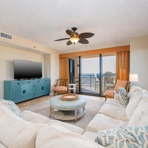 This spacious living area features a large sectional sofa, a flat-screen TV, and a stunning beachfront view from the balcony