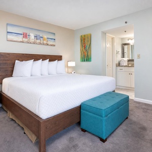 The master bedroom features a plush king bed, vibrant artwork, and a stylish turquoise ottoman, creating a relaxing retreat