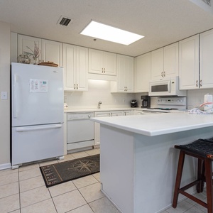 Bright white cabinetry complements the kitchen's sleek design, featuring a breakfast bar with stylish seating and beach decor