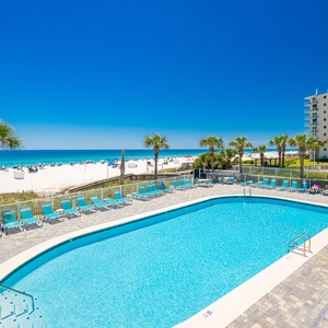 Relax on the balcony by the sparkling pool surrounded by palm trees, with inviting beach access just steps away