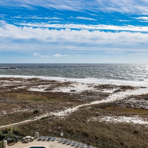 Expansive view of the beach with waves lapping against the shore and the jetties in the distance, framed by lush greenery