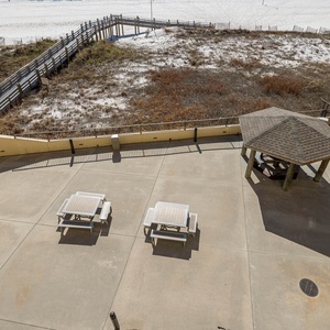 Overlooking the pool area with picnic tables and a gazebo, leading to a beach front with white sand and a wooden walkway