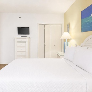 Brightly decorated guest bedroom featuring a queen bed, a flat-screen TV, and a charming lamp beside a colorful painting
