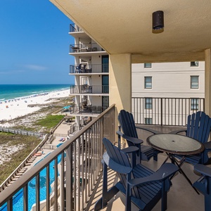 A private balcony features turquoise chairs and a glass table, offering a serene view of the tranquil beach and blue skies