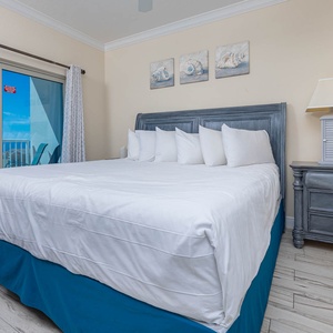 The master bedroom features a plush bed with white linens and a stunning beach view through large sliding glass doors