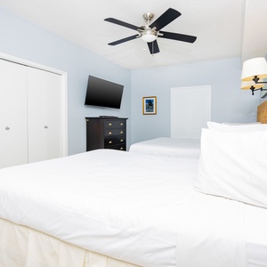 Guest bedroom featuring two double beds, a wall-mounted TV, and a stylish woven headboard against soft blue walls