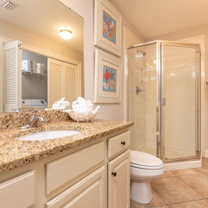 The extra bath features a stylish granite countertop, a glass walk-in shower, and a laundry closet with a washer and dryer