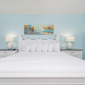 Brightly colored artwork complements the serene blue walls in the master featuring a plush king bed and stylish lamps