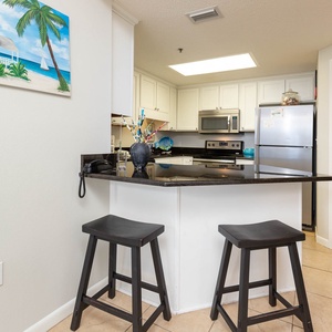 The breakfast bar with stools overlooks an inviting kitchen featuring sleek stainless appliances and vibrant decor