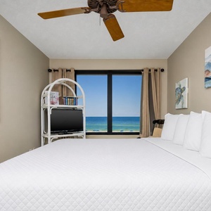 This bedroom features a large bed, a TV, and a stunning beachfront view framed by elegant curtains