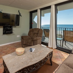 This inviting seating area features a plush recliner, wall-mounted TV, and stunning beach views through large glass doors