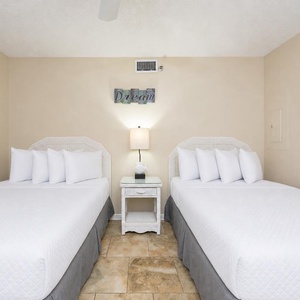 Bright guest bedroom featuring two double beds, a bedside table, and cheerful artwork, creating a welcoming atmosphere