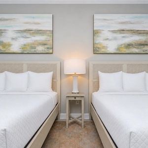 Rest in this guest bedroom featuring two queens, soothing artwork, and coastal vibes