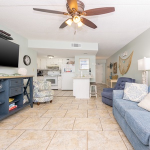 The living area features a large TV, comfortable seating, and a view into the bright kitchen, perfect for relaxation