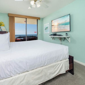 Brightly colored walls frame a cozy master bedroom featuring a king bed, a mounted TV, and a balcony with a beach view