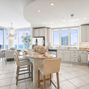 This kitchen features elegant white cabinetry, granite countertops, and a stunning beach view from large windows