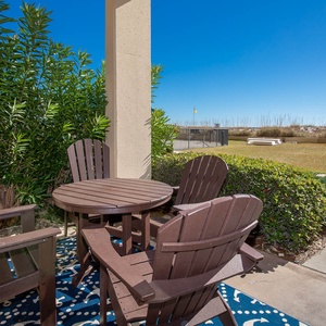 Cozy outdoor patio area features a round table and four wooden chairs, surrounded by lush greenery and a clear blue sky
