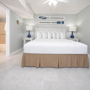 The inviting bedroom features a king bed with decorative pillows, stylish blue lamps, and a bathroom entrance nearby