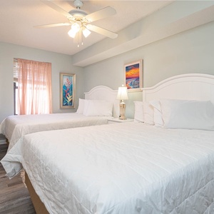 This guest bedroom features two comfortable double beds, colorful artwork, and a cozy atmosphere enhanced by natural light