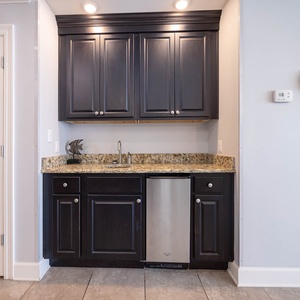 Prepare drinks or snacks at the stylish wet bar, featuring granite countertops, dark cabinetry, and an ice maker