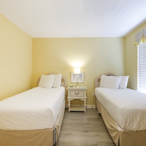 Guest bedroom featuring two twin beds, a bedside table with a lamp, and cheerful yellow walls