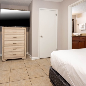 Guest room featuring two double beds, a large dresser, and a wall-mounted TV, with a doorway leading to the bathroom