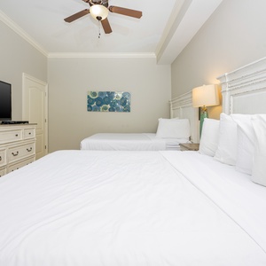 This guest bedroom features two comfortable queen beds, a large TV for entertainment, and a vibrant wall art piece