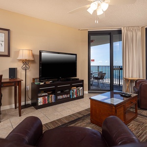 Cozy living area features a large TV, a comfortable brown recliner, and access to a balcony with a view of the gulf
