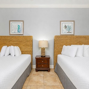 Inviting guest bedroom featuring two queen beds with woven headboards and coastal artwork