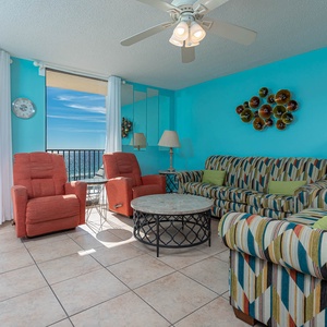 Vibrant living area features striped sofas with a queen sleeper, red recliners, and a stunning balcony beach view
