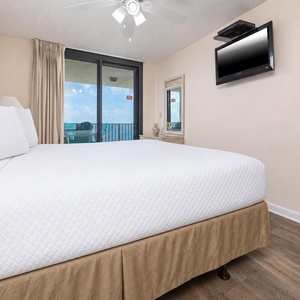 Relax in the master bedroom with a plush king bed, a TV, and sliding doors that lead to a balcony with beach views