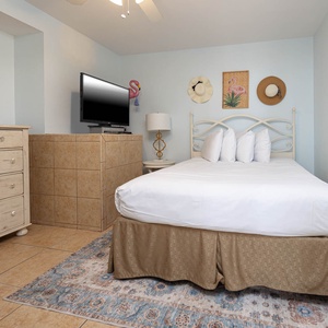 The guest bedroom features a queen bed with decorative pillows, a TV, and a stylish dresser against a soft blue wall