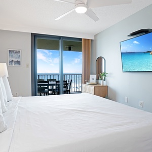 Serene master bedroom features a king bed, a wall-mounted TV, and sliding doors leading to the balcony with a beach view