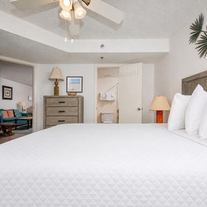 A comfortable bedroom features a large king bed with plush pillows, a stylish dresser, and a cozy sitting area visible